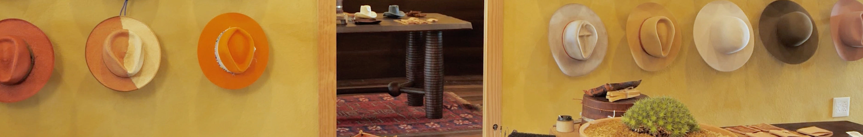 Collection of wide-brimmed hats in shades of orange, beige, and brown, showcased in a warm, rustic interior.