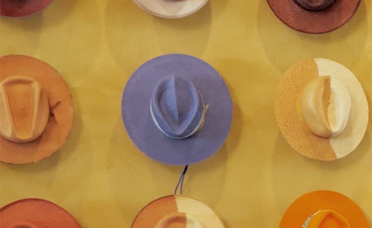 Collection of colorful hats, including purple, orange, and straw, hanging on a yellow wall.