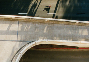 Aerial view of a person lying on a skateboard with palm trees casting shadows.