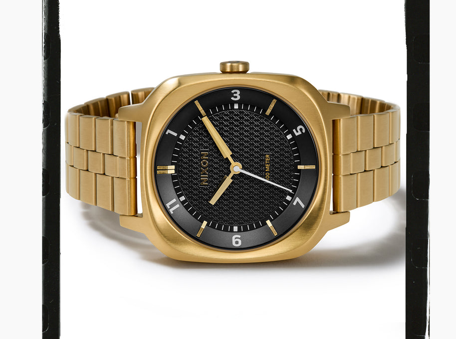A gold-tone metal wristwatch with a black textured dial, gold-tone bezel, and matching gold-tone link bracelet, shown on a white background.